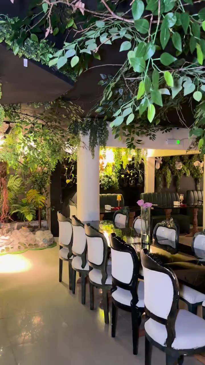 Salón de Almonte Restobar con sillas blancas, mesas de mármol negro y techo cubierto de hojas